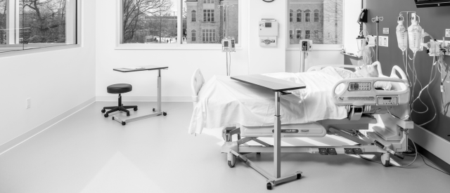 一个现代人的单色照片, empty hospital room with a bed, various medical equipment, 还有一扇可以俯瞰外面建筑的大窗户.