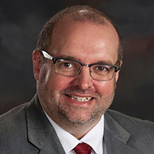 Professional man with a friendly smile wearing glasses, a dark suit, and a red tie.