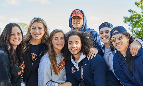 A group of cheerful young adults wearing team apparel, showcasing school spirit and camaraderie on a sunny day.